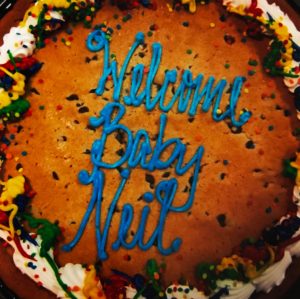 A photo of a cookie cake that Everett's Aunt Jen and Uncle Casey brought to the hospital after he was born. It has colorful icing and blue letters that read "Welcome Baby Neil"