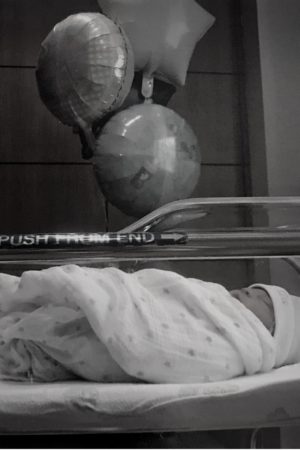 Newborn Everett lying in his hospital bassinet with some "baby boy" balloons in the background