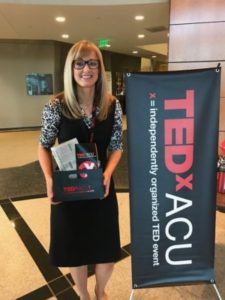 A picture of me standing next to a TEDxACU banner holding all of my swag!