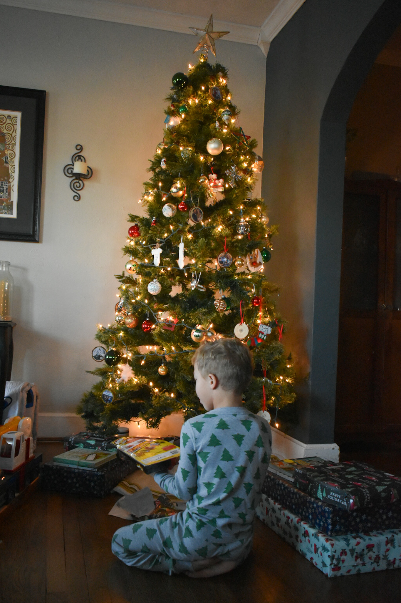 One little boy opening up presents by the family tree